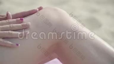 一位苗条的年轻女子在沙滩特写镜头下，用<strong>防晒喷雾</strong>在双腿上晒太阳。夏季休闲。身体护理